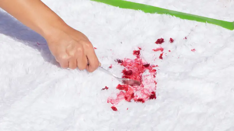 A person's hand spreads red cranberry sauce with a spoon on a white shag rug