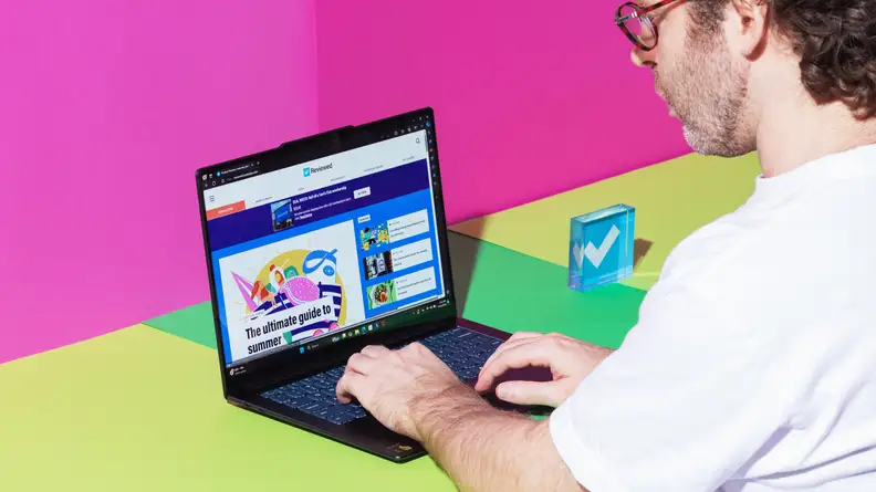 A man typing on a Lenovo Yoga Slim 7x laptop on a pink background.