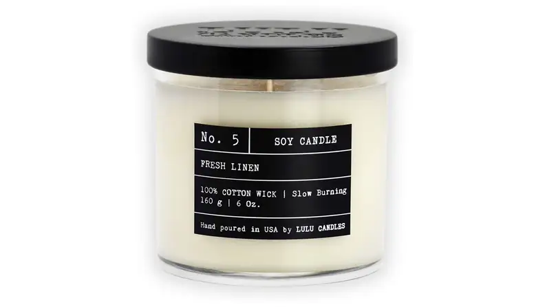 Product shot of white candle with black label and lid.