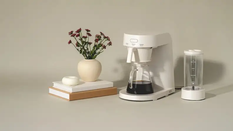 White Ratio coffee maker with a glass carafe beside a vase of flowers