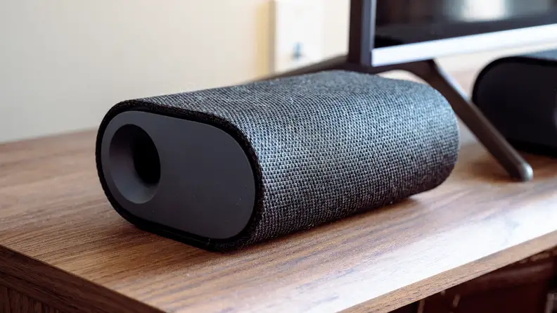 A black surround sound speaker sits on a wooden table.