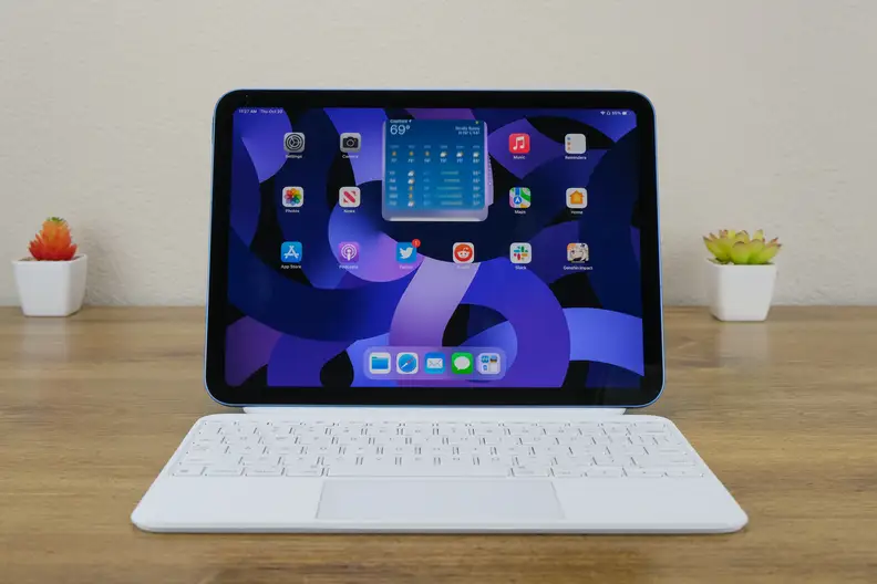 The Apple iPad 10 sits on a wooden desk with its white keyboard facing forward.