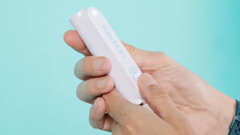 A person holding the remote to the HigherDose Red Light Face Mask.