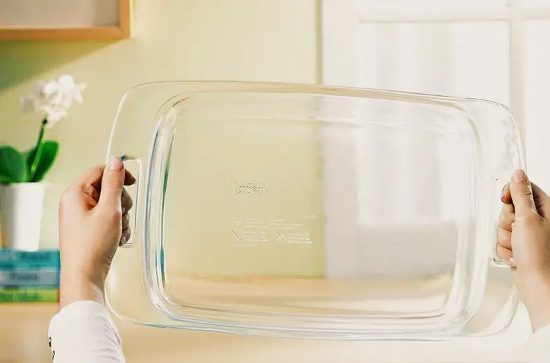 A person holds a clean rectangular Pyrex dish up to the light.