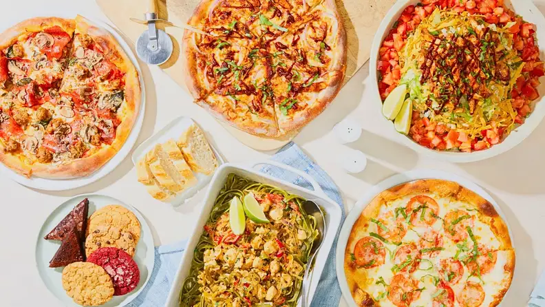 An assortment of CPK pizzas, pasta, bread, and desserts on a table