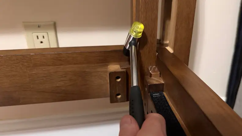 Wooden joinery bed frame shown being assembled using a yellow-tipped rubber mallet.