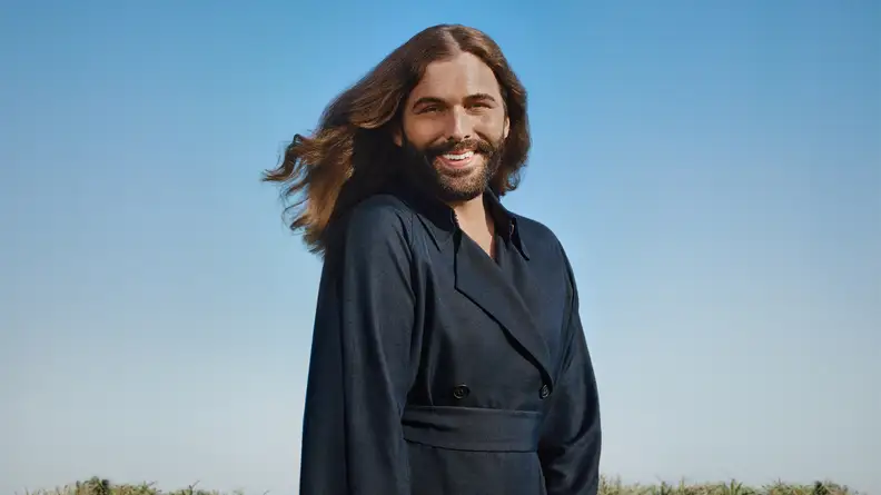 Jonathan Van Ness stands against a sky in the background.