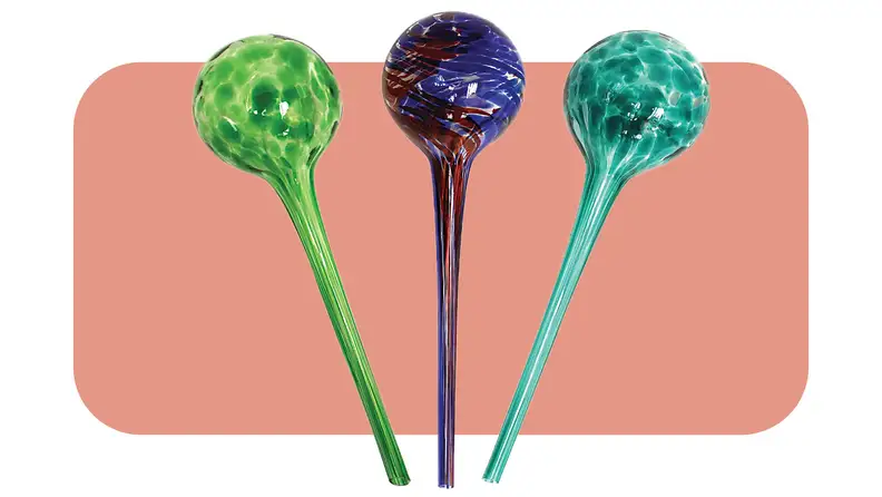 Set of three glass watering globes in green, red and blue and turquoise colors in front of pink background.