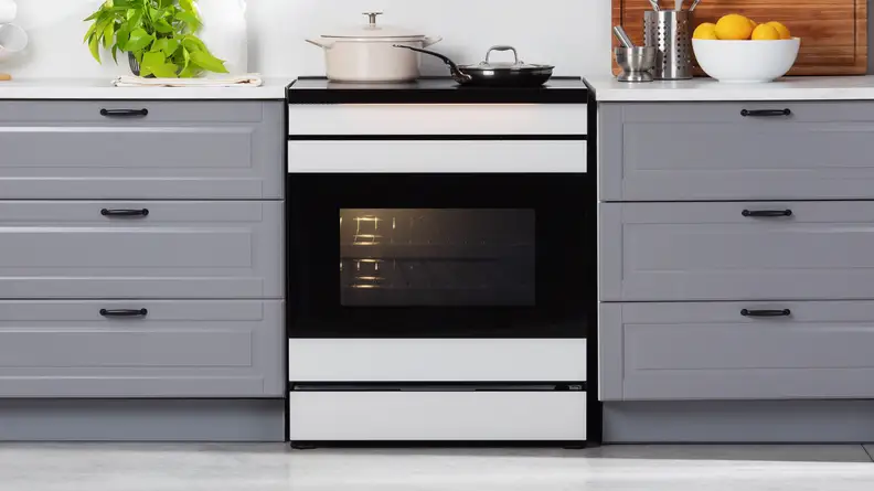 The Samsung Bespoke NSI6DB990012AA Induction Range in a modern kitchen setting nestled between two cabinets with the range's interior light on.