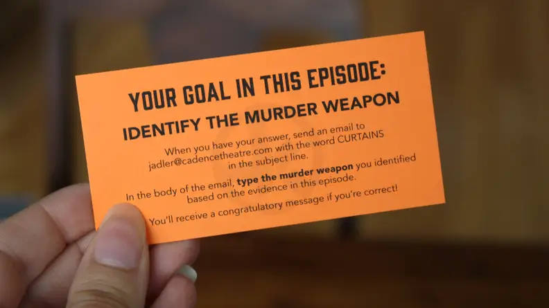 Hand holding an orange card from Hunt A Killer