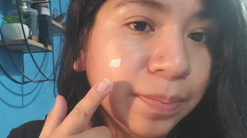 The author's face as her hand reached up and applies a dollop of white cream on her cheek.