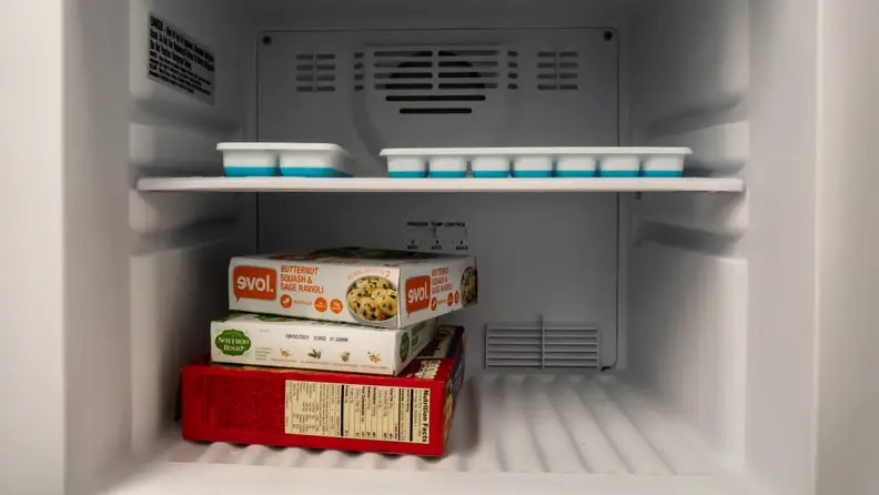 A close-up of the freezer compartment, with a few boxes of frozen food added for scale. A frozen pizza box takes up the entire width of the freezer.