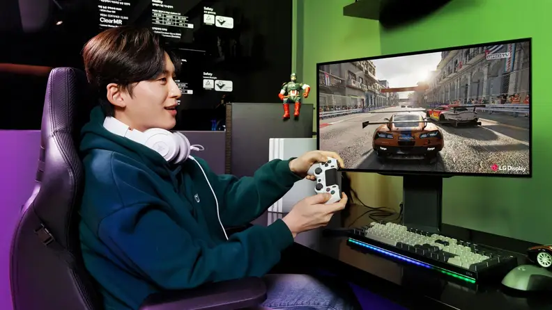 Person sitting at desk in front of LG desktop monitor while excitedly using a controller to play video game on screen.