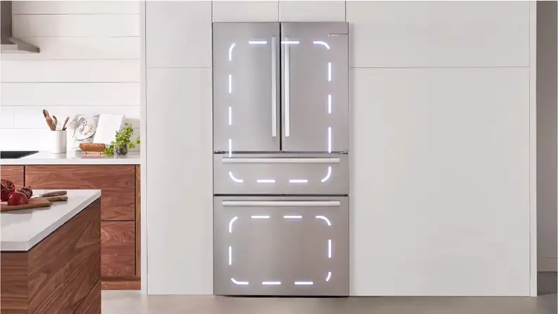 A close-up of a Bosch French-door fridge with a flex drawer, installed in a modern kitchen. There are dotted lines highlighting the two different compressor zones, one that covers the fridge compartment and flex drawer and one that just covers the freezer.