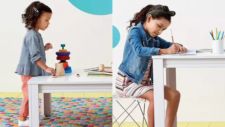 A toddler plays at her art table while an older child does work at her desk.