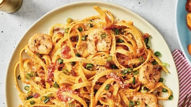 A plate of pasta with shrimp, tomatoes, and green onions
