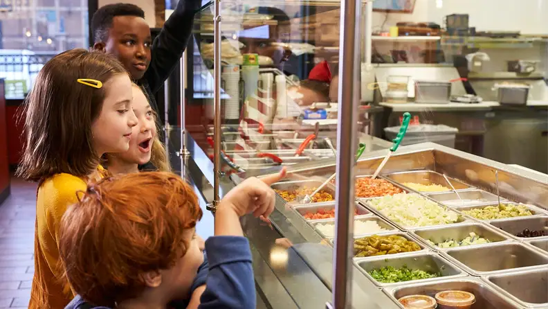 Kids pointing excitedly at food options behind a serving counter