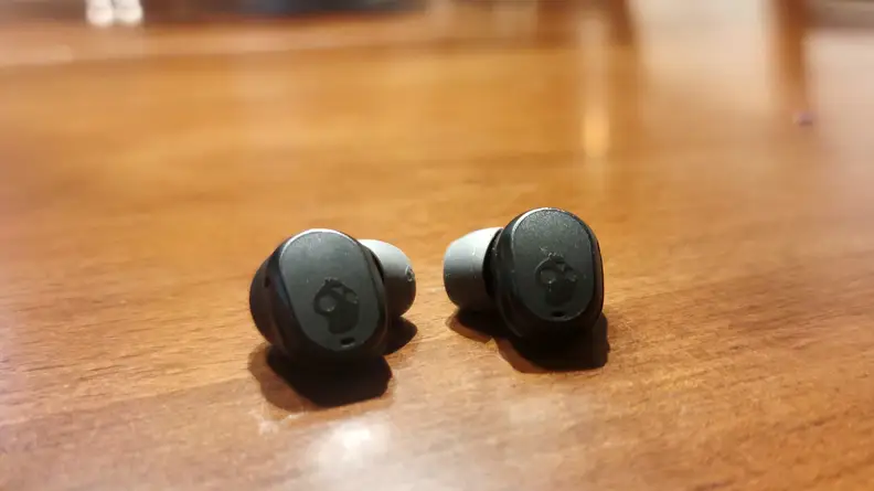 The all-black Skullcandy Mod earbuds sit on a wooden cabinet