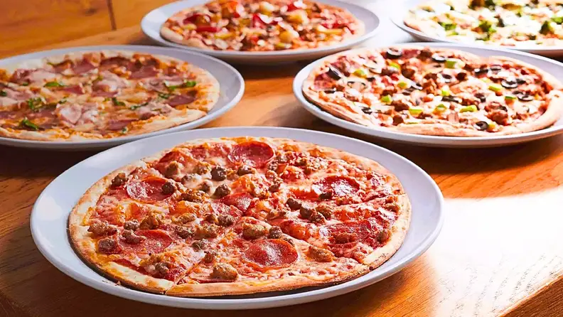 Several different pizzas displayed on plates on a wooden table