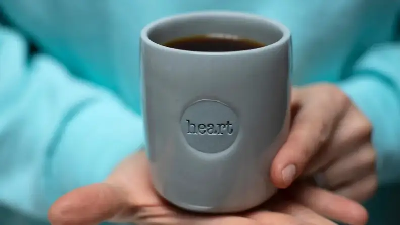 Hand holding a gray mug stamped with the word heart