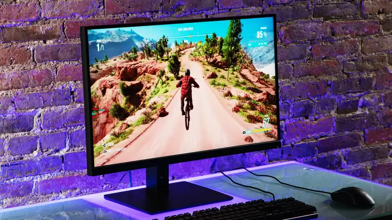 Destop monitor with animated game on screen in front of brick wall sitting on top of desk with keyboard and mouse.
