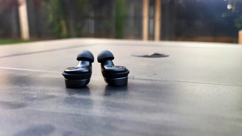 The graphite Sennheiser Momentum True Wireless 3 earbuds sit facing up on on a black table.