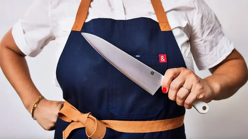 Person wearing navy apron and holding chef's knife from Hedley & Bennett.