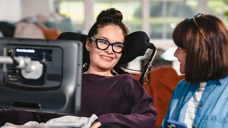 A woman in a wheelchair using an AAC device while conversing with another woman