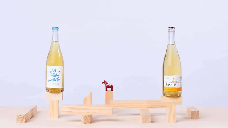 Two bottles of white wine perched on an elevated wooden platform against a white background.