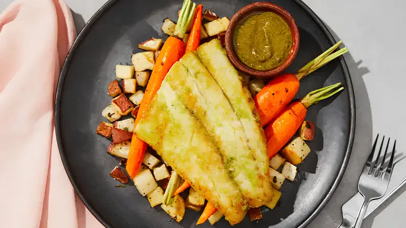 Prepared meal for one person with grilled fish, roasted carrots, potatoes, and sauce, plated as a balanced single-serving dish.