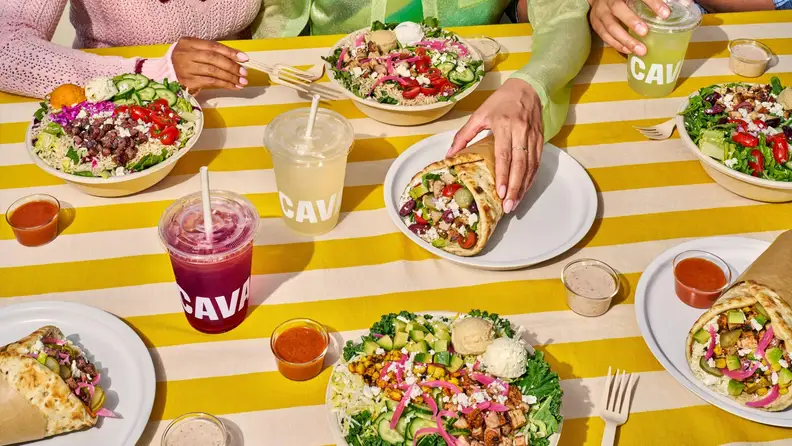 People at a table with CAVA bowls, pitas, dips, and drinks