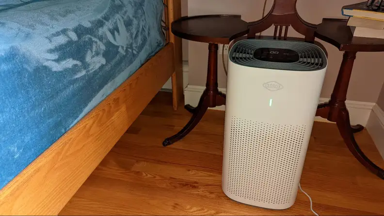 The air purifier hooked up and placed on the corner of a bedroom.