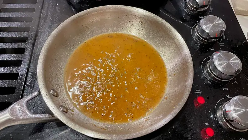 Leftover fond inside a stainless steel pan on a black stovetop.