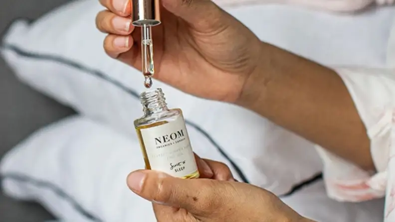 a woman fills a dropper with Neom Organics Sleep Face Oil