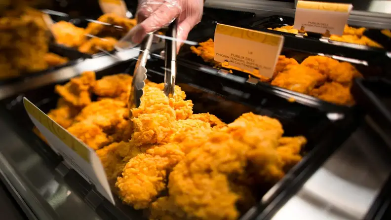 Close-up of tongs picking fried chicken tenders from a deli case