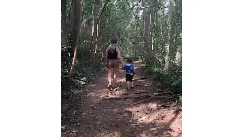 Adult and child walking hand in hand along a forest hiking trail.