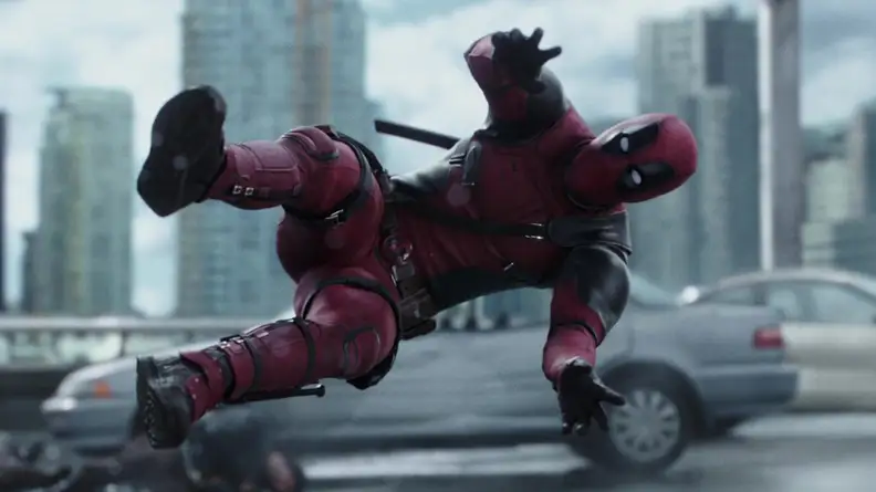 Deadpool (Ryan Reynolds) being launched into a car with a city skyline in the background.