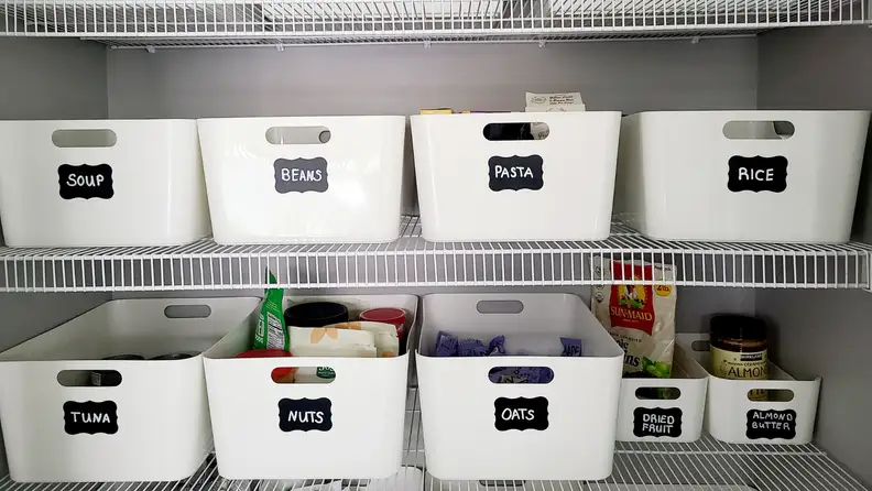 White organization bins with black chalkboard labels inside of a kitchen pantry of home.