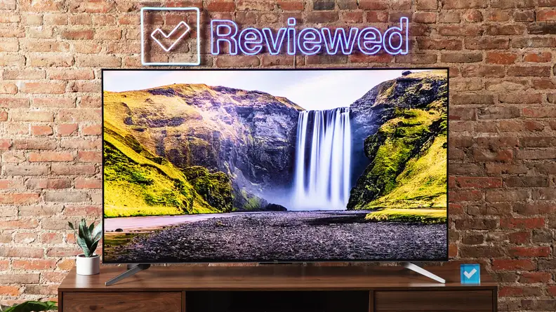 The TCL Q7 TV on an entertainment center with a brick background.