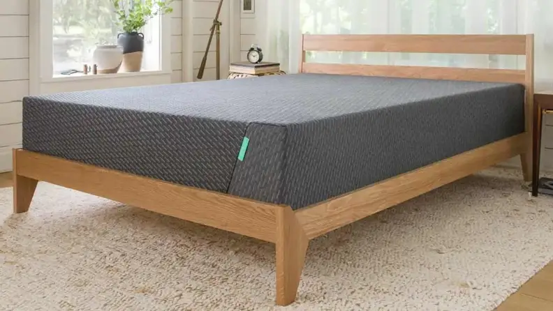 A Tuft & Needle Mint mattress on a frame in a bedroom.