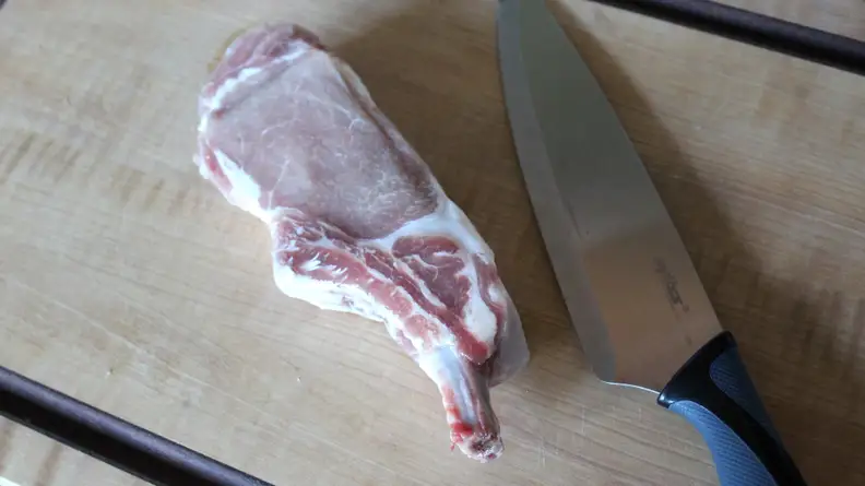 In the center of the cutting board, there's a piece of uncooked Kurobuta pork chop and a knife.