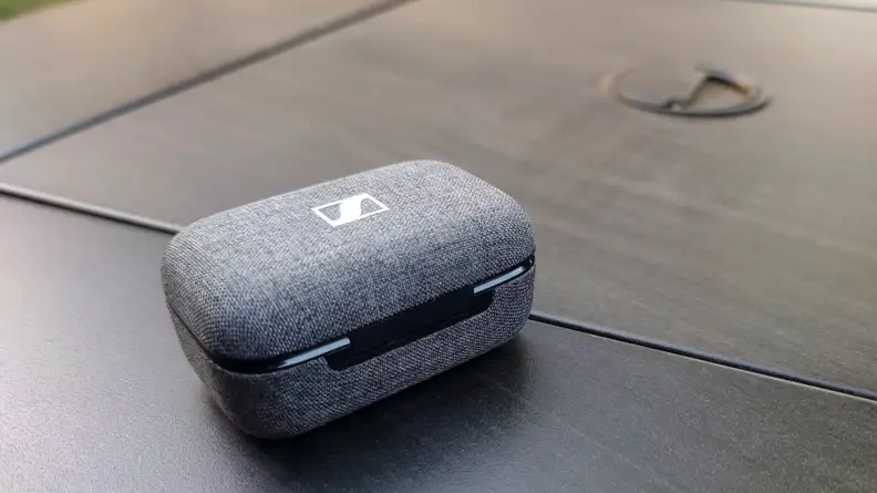 The grey fabric Sennheiser Momentum True Wireless 3 case sits on a black table.