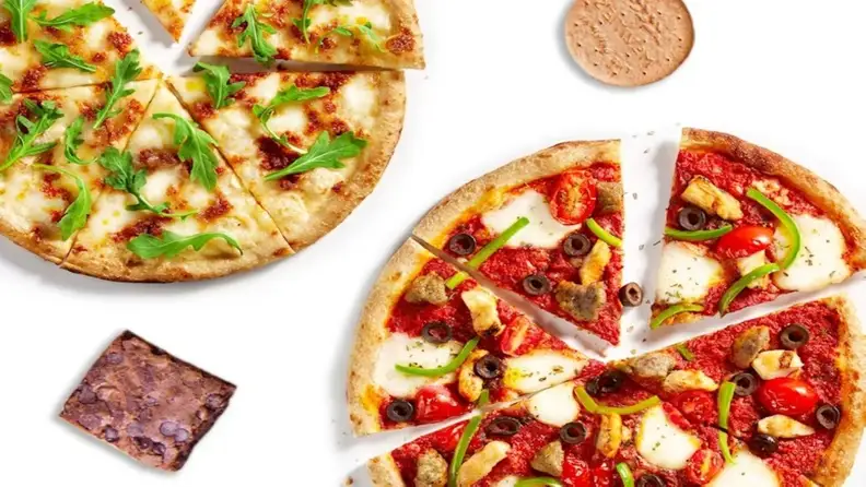 Two personal pizzas, one with arugula and one with veggies, next to a brownie and cookie