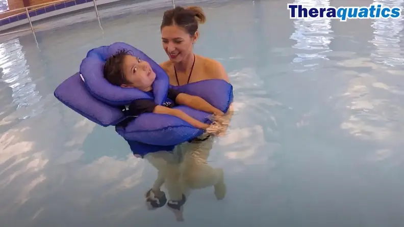 A boy wearing a floatie in the water with the support of his mother.