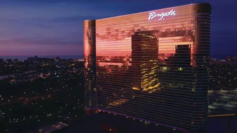 A hotel towering over the surroundings with its glass exterior reflecting the city during the evening
