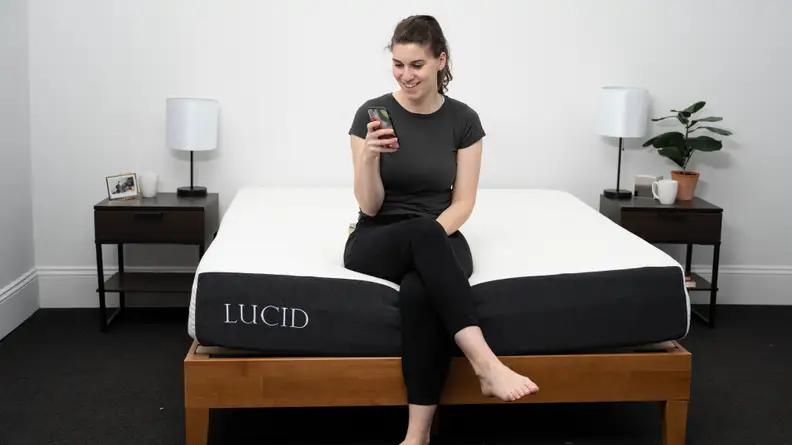 a person sits on the edge of the lucid mattress looking at their phone