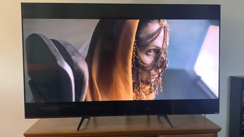 TCL 5-Series TV displaying movie on top of wooden credenza.