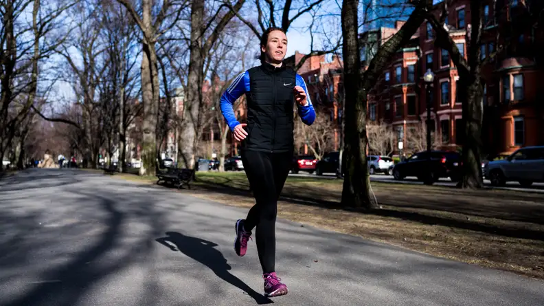 A woman running down the street wearing a Nike vest.