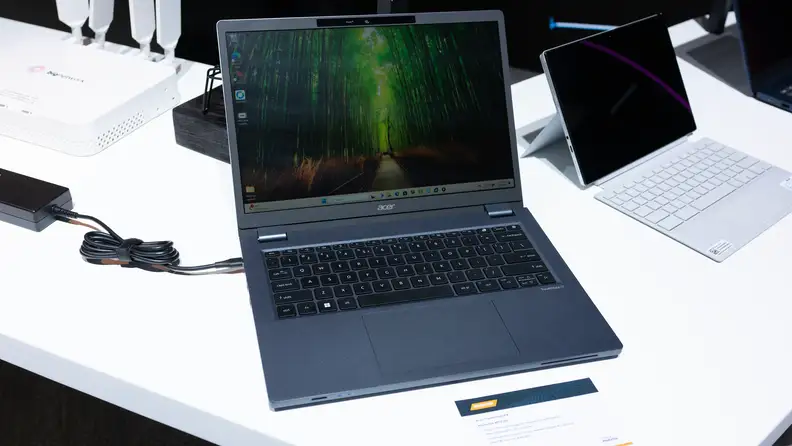 The Acer TravelMate P4 open on a table displaying a forest scene.