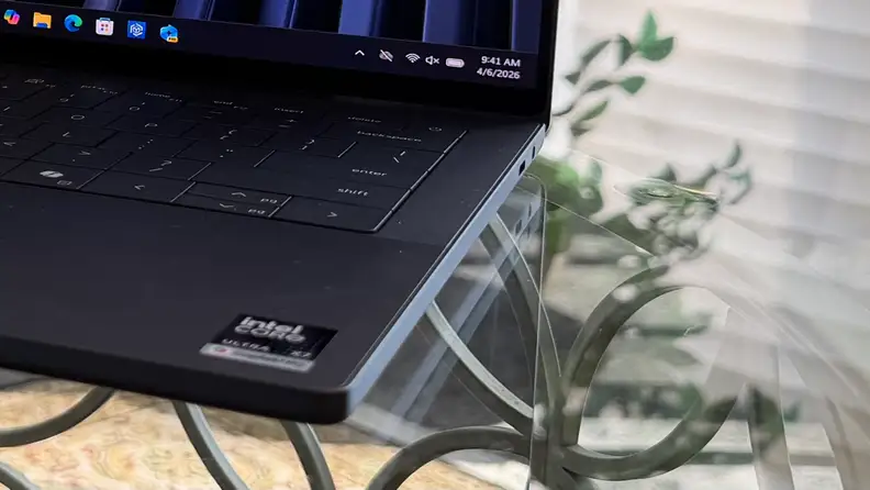 Close-up photo of side of Dell XPS 14 2026 laptop showing ports, atop a glass table with green plants in the background.